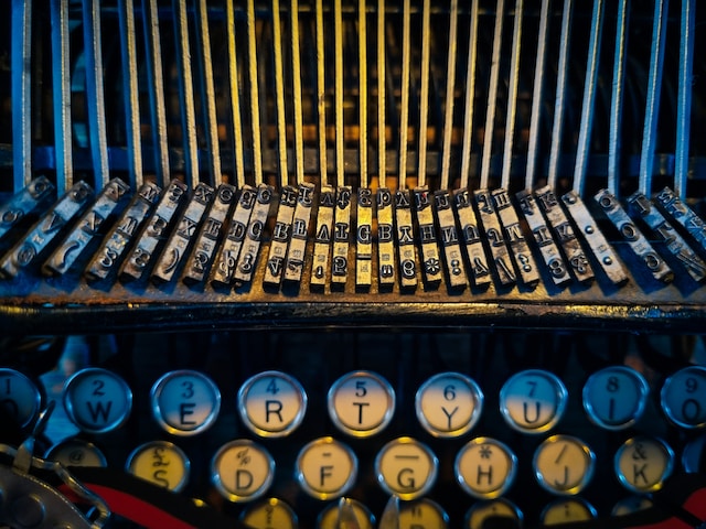 Landscape close up image of a typewriter. Typebars (also called strikers) are shown in the top two thirds of the picture, with two rows and a partial row of keys in the bottom third of the picture.